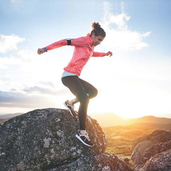Female runner jumping down from a rock